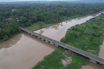 Aerial view of the long bridge over the brown watery river. the river delta is overgrown with green...