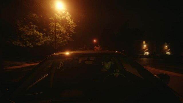 Dangerous male caucasian killer driving in the night and escaping. Dramatic, moody with a red tint. Windshield POV Wide Shot. American streets.