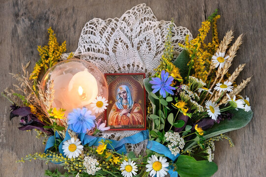 old orthodox icon with Our Lady image, candle, sacred herbs and flowers on wooden table. ritual prayer. Herbal consecration - traditional customs on August 15th, Assumption of Mary day. top view