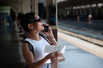 Young beautiful woman wear sunglasses using smartphone at  Hua Lamphong station in Bangkok, Thailand