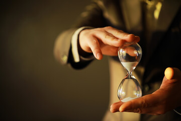 Businessman holding an hourglass isolated on dark background - time is money concept.