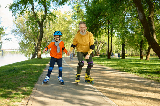 Happy senior man and little boy rollerskating in urban park