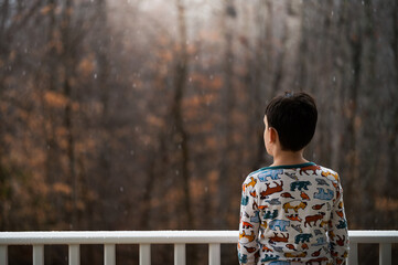 A boy watching the snow fall on the front porch
