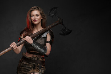 Stunning Viking girl dressed in a chainmail top and fur skirt posing with axe
