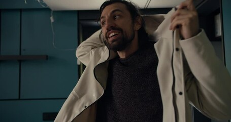 A brunette guy in a white jacket takes off his outerwear after a walk in the fresh air. Rest in a warm house during cold weather