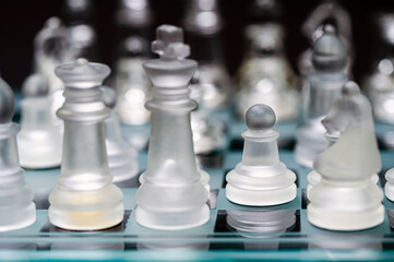 glass, transparent chess pieces on a checkerboard, selective focus, close-up, isolated on black