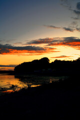 Sunset landscape over the water reflecting the sunset in the sea. behind the clouds and the blue sky over the lagoon.A beautiful panorama of the sky with glowing clouds.Red sun. river.	