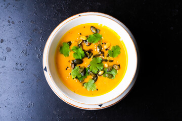 Pumpkin and carrot soup with cream and parsley on dark wooden background