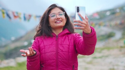 Portrait of excited young Indian woman talking on video call with vivid expressions. Girl connects with family with smart phone. Tourist making vlog in mountains.