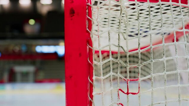 Ice hockey goal in close up orbiting dynamic shot. Vibrant red posts with dirty nets.