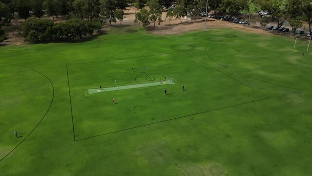 Boys practice cricket on Perth City training field in Australia, aerial circling view