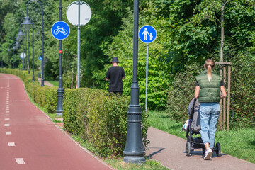 Young blonde hair girl or mother with baby carriage, pram or stroller walking near the bike road...