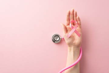 Honor Breast Cancer Awareness Month with this top view image of female hand holding pink ribbon and stethoscope on pastel pink isolated background with copyspace available for text or ads - Powered by Adobe