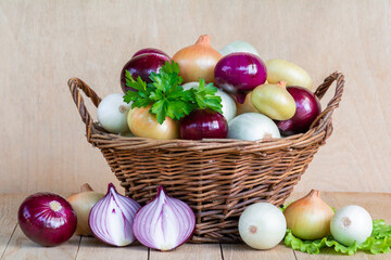 Onions of different colors in a wicker basket on a wooden table. A mix of onions of different colors