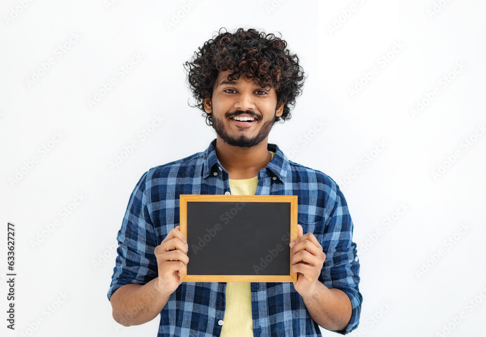 Wall mural Happy Asian man with curly hair holds a small empty chalkboard looks at the camera and smiles friendly standing on a white background