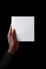 A human hand holding a blank sheet of white paper or card isolated on black background