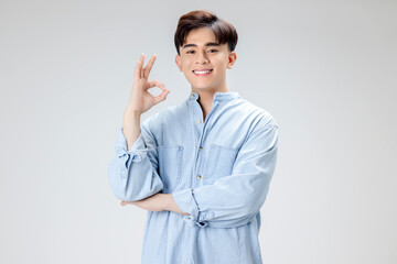 Happy young Asian smart man shows OK hans sign over isolated background.