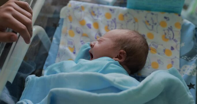 A newborn boy yawns lying in a cradle for babies in the maternity hospital