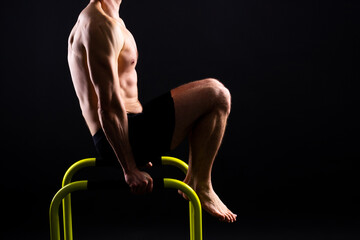 Young muscular man doing parallel bar exercises in dark white red studio with copy space