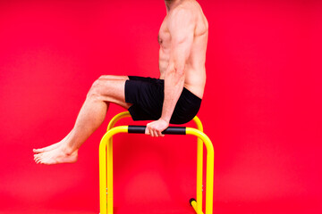 Young muscular man doing parallel bar exercises in dark white red studio with copy space