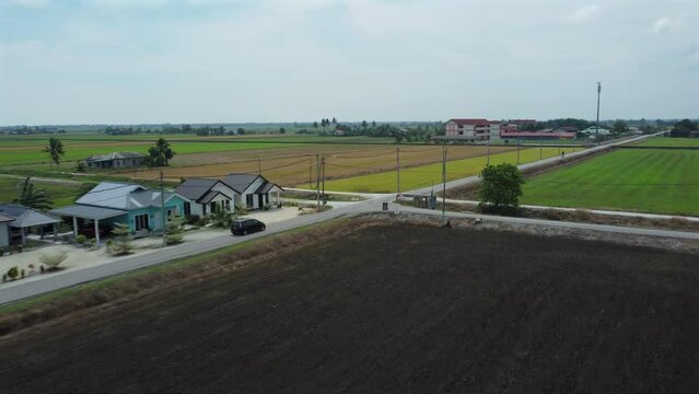 Side follow shot of a car moving surrounded  with green paddy fields crossing an intersection