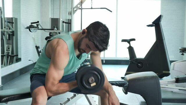 In the gym, a health-conscious male readies for exercise with dumbbells at the gym, a healthy lifestyle at the fitness gym, a Middle Eastern male 25-year-old man