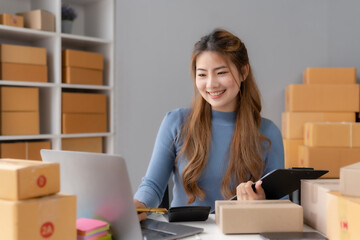 Young Asian female ecommerce business owner prepares package box for customer and delivery check...