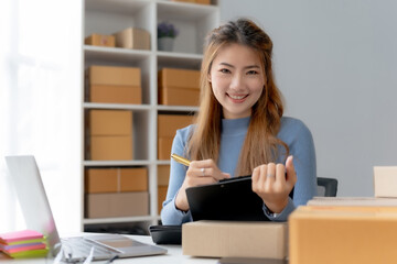 Young Asian female ecommerce business owner prepares package box for customer and delivery check balance. SME. Preparing products and inspecting products before sending to customers.