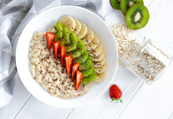 Colorful vitamin breakfast of oatmeal with fresh fruits, strawberry, banana, kiwi and linseeds. Recipe of healthy meal, clean eating, balanced nutrition.