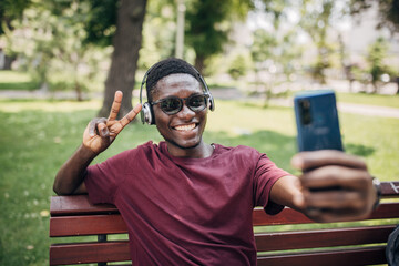 Young African American man sitting on a park bench, taking a self-portrait with a smartphone