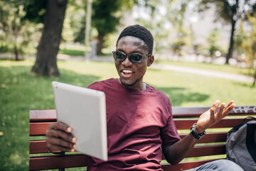 Fototapeta premium Young man sitting in the park relaxing in the nature and using digital tablet