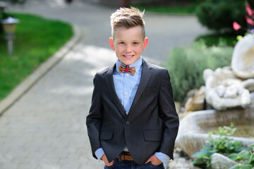 Fashion kid boy in suit and bow tie. Portrait of kid in spring park outdoors. Close-up face child playing outdoors in summer park.