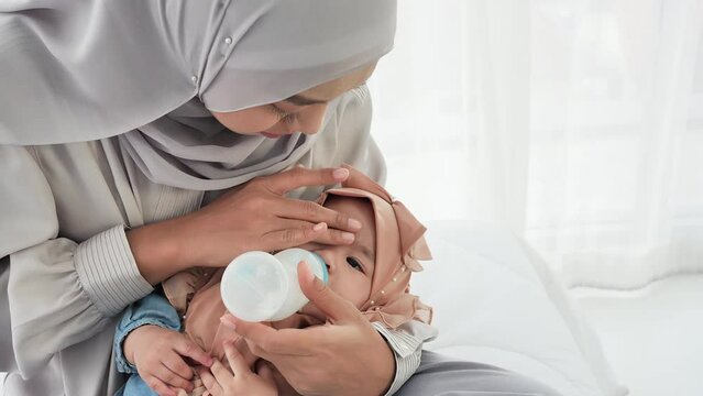 Nurturing Bond, In a tender moment, a mother lovingly carries her baby girl, aged 6 months, while she drinks milk from a bottle in her home, embracing a bond of love and care. slow motion shot