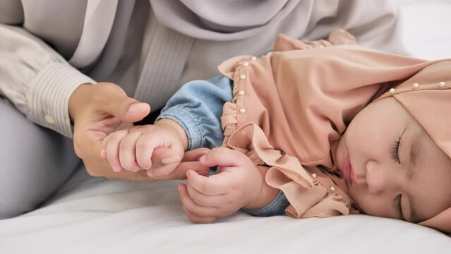 Soothing Bond, In tender moments, a mother tends to her holding hand sleeping baby girl, fostering a strong bond of protection, care, and boundless love. Muslim, 6-month-old baby girl. slow motion