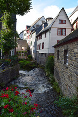 Half timbered (timber frame) houses in the village of Monschau, Eifel, Germany - picturesque village with river Rur - red flowers in front of view