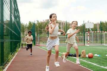 Active schoolgirl in white sportswear leading in running competition while moving along race track...