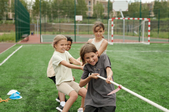 Group of strong and active schoolchildren making effort while pulling rope during school sports competition with more powerful team at stadium