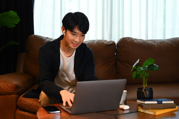 Handsome male in smart casual wears browsing internet, remote work or stying online on laptop at home