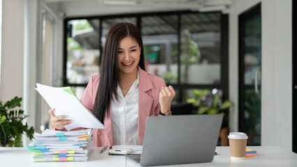 A cheerful Asian businesswoman looking at her laptop screen with an excited and happy face