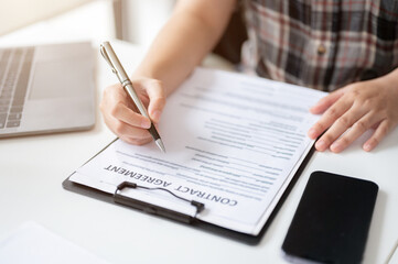 Close-up image of a woman signing her signature on a contract agreement at a table.
