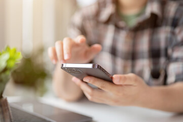 Close-up image of a female in a flannel shirt using her smartphone at a table.