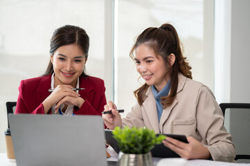 Two Asian businesswomen are looking at a laptop screen, discussing and planning work