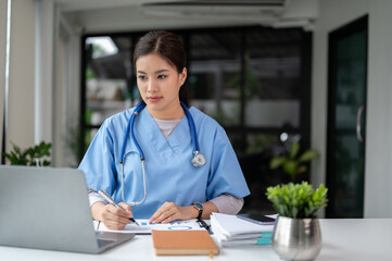 A professional Asian female doctor is working and reading medical research on her laptop
