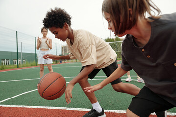 African American schoolboy in activewear dribbling ball while running forwards in front of his...