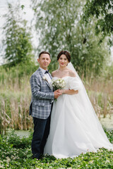 Newlyweds couple are standing on the shore of a lake. The bride and groom embrace and hold hands in nature. A love story. Happy wedding day of marriage. Getting married outdoors.