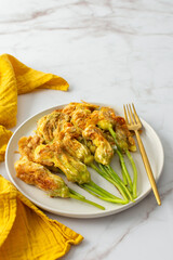 Fried zucchini flowers in batter, plate with zucchini flowers on marble background