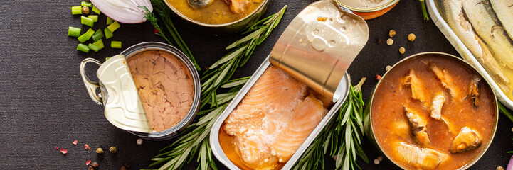 Different open tin cans with canned fish among spices and herbs banner, canned salmon and mackerel,...