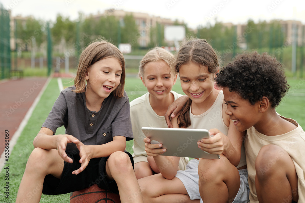 Poster group of happy intercultural classmates in activewear watching online video while looking at screen 