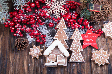 Christmass New Year decorations. Hollly berries, sweet Christmas gingerbread cookies in shape of house and Christmas trees on wooden background.
