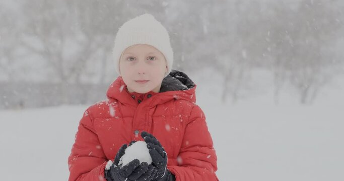 Boy makes snowball and throws in the camera. Teenage boy in red jacket playing snowballs in park. Active entertainment in winter.